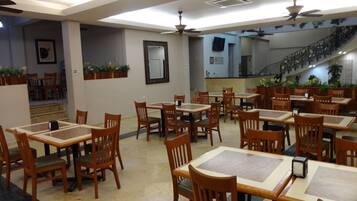 A restaurant with multiple wooden tables and chairs, ceiling fans, and potted plants.