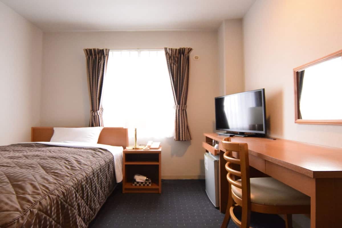 Ein Hotelzimmer mit einem Bett, einem Schreibtisch mit Fernseher und einem Sessel.