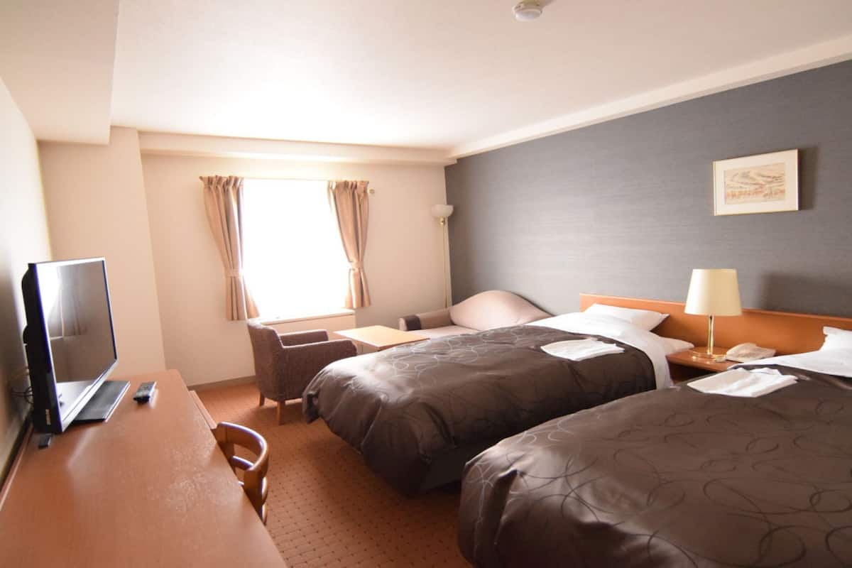 Ein Hotelzimmer mit zwei Betten, einem Schreibtisch mit Computer, einem Stuhl, einer Lampe und einem Fenster mit Vorhängen.