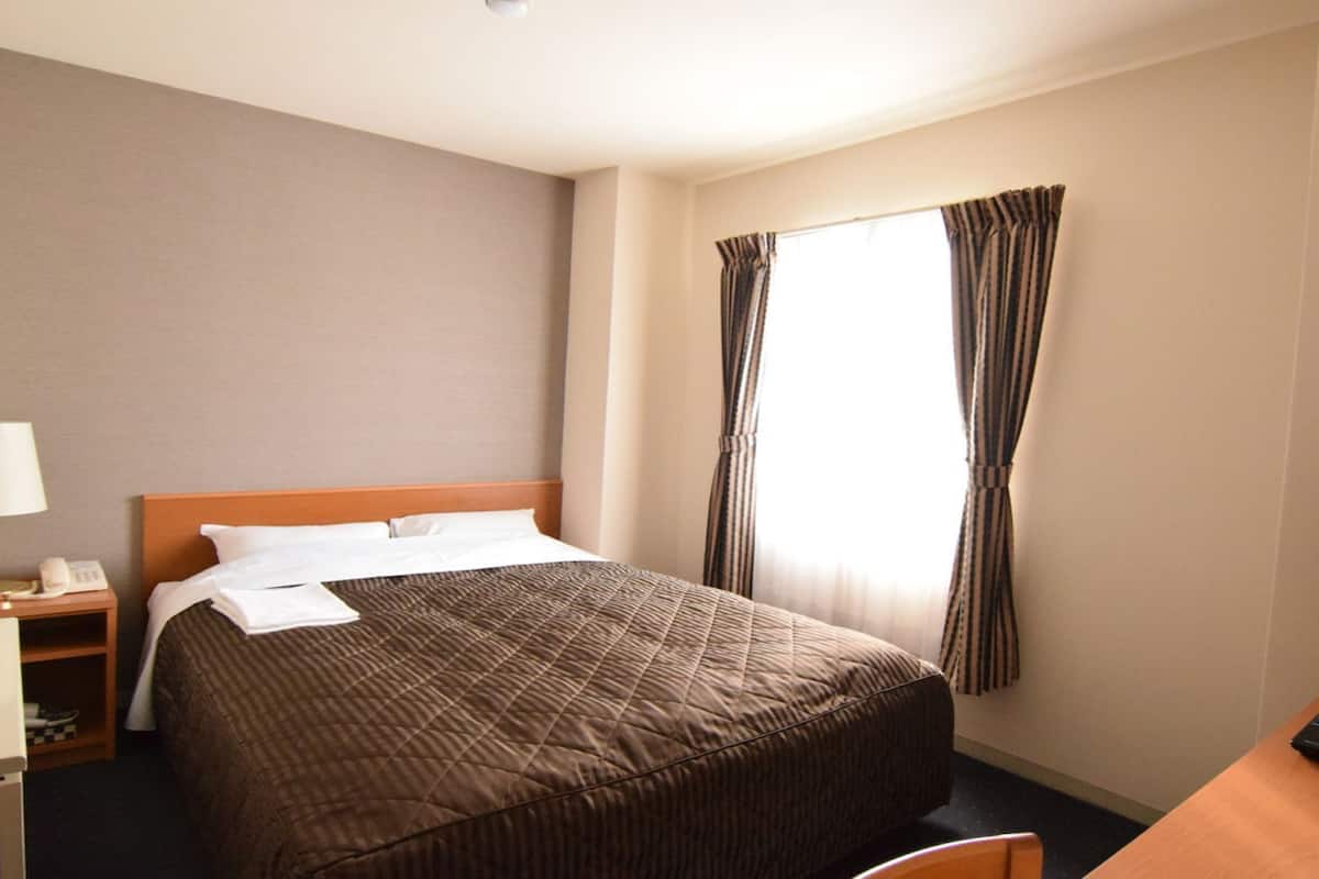 Ein Hotelzimmer mit einem Bett, einem Schreibtisch, einer Fernbedienung, einer Lampe und einem Telefon.