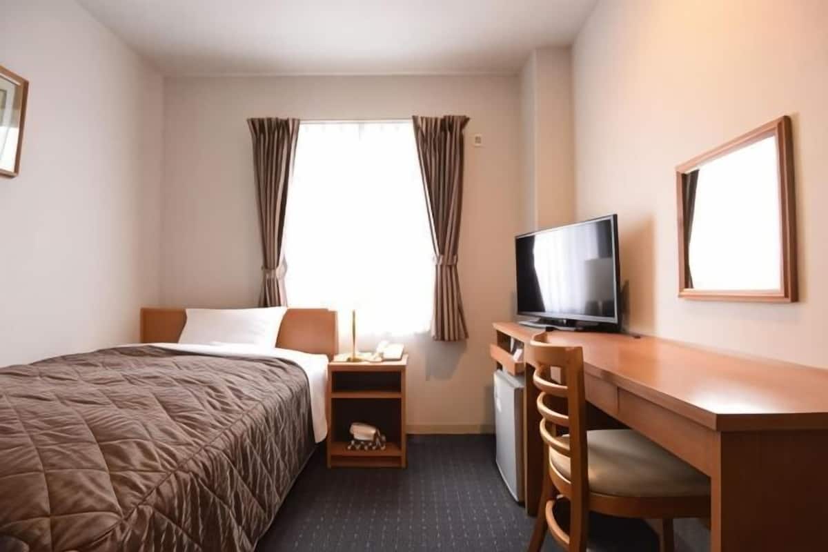 Ein Hotelzimmer mit einem Bett, einem Schreibtisch mit Fernseher, einer kleinen Sitzecke und einem Fenster mit Vorhängen.