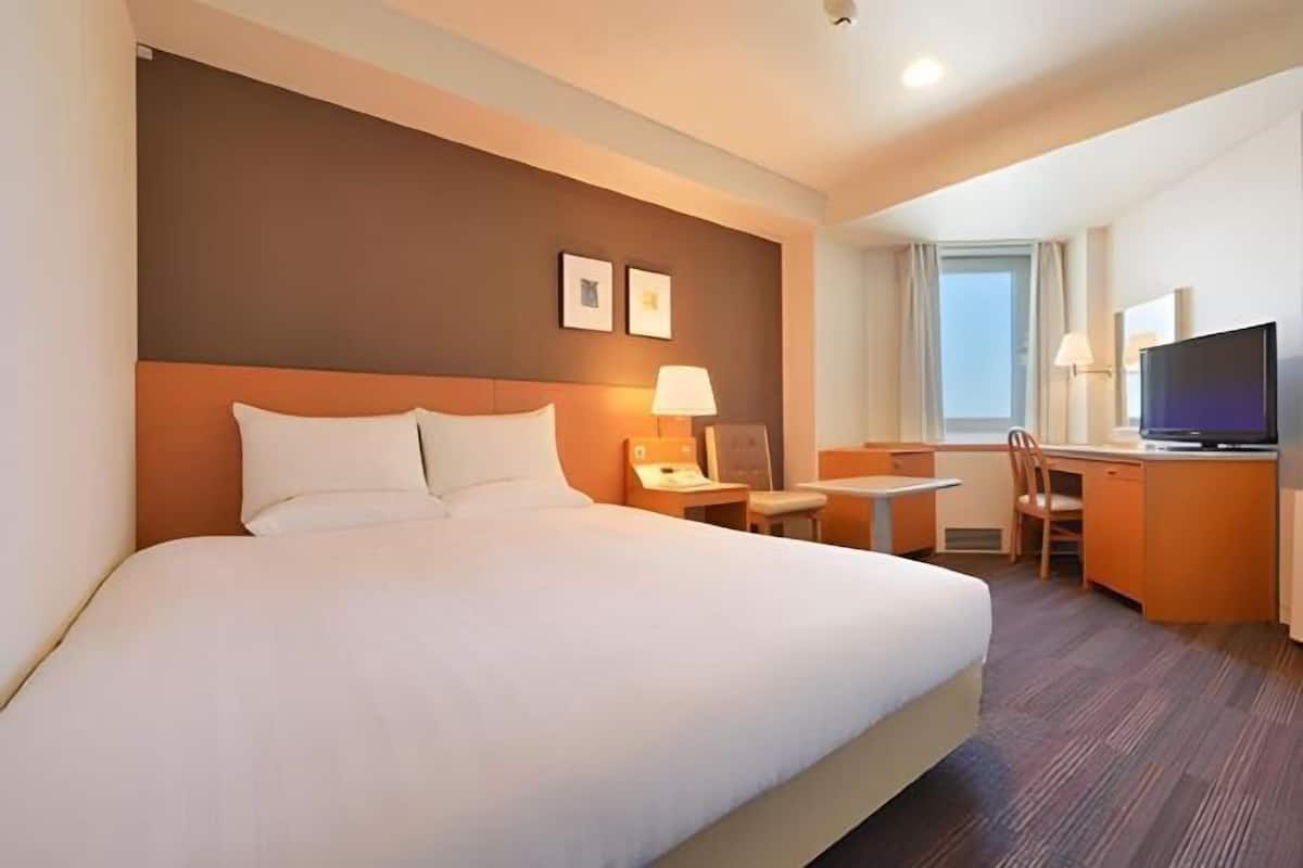 Ein Hotelzimmer mit einem großen Bett, einem Schreibtisch mit Stuhl, einem Fernseher und einem Fenster.