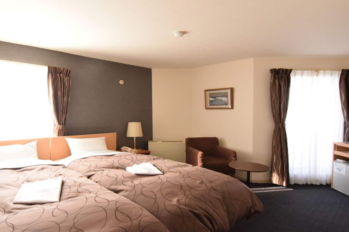 Ein Hotelzimmer mit einem großen Bett, zwei Nachttischen, einem Sessel, einem kleinen Tisch und einem Bild an der Wand.
