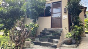 A villa with a wooden door, a staircase leading to the entrance, and a sign indicating the villa name and number. - Villa Anjing 2 (Nusa Dua)