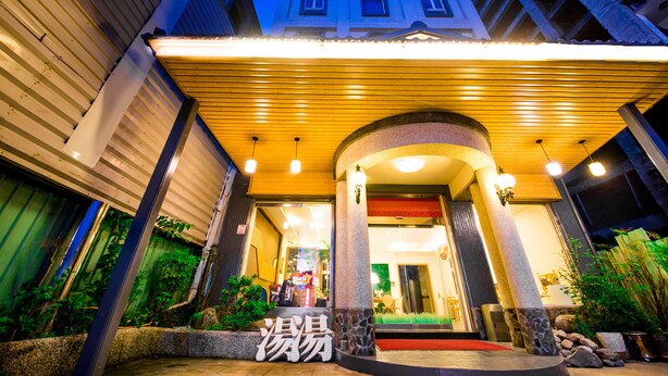L’entrée d’un hôtel, avec une allée couverte, des piliers en pierre et un tapis rouge menant à l’intérieur.