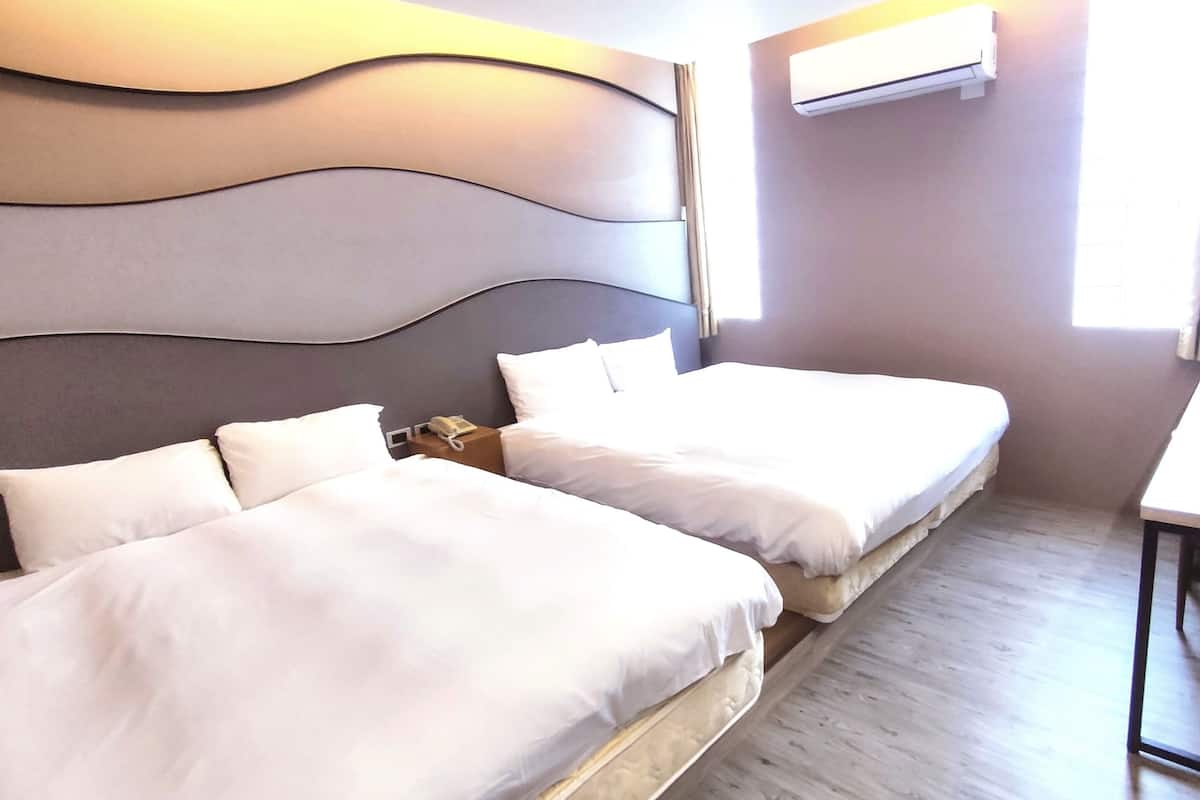 A hotel room with two beds, a bedside table with a phone, and an air conditioning unit on the wall.