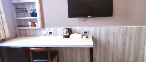 A small kitchenette with a flat-screen TV mounted on the wall, a coffee maker, and a shelf with kitchen essentials.