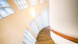 Un escalier en colimaçon doté d’une rampe en bois, qui monte à travers un bâtiment aux grandes fenêtres laissant entrer la lumière naturelle.