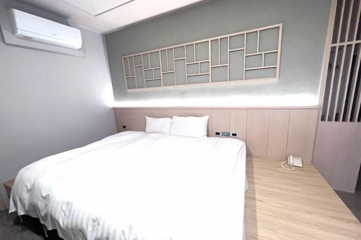 Habitació d'hotel amb un llit gran, aire condicionat fixat a la paret, terra de fusta i un telèfon integrat.