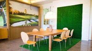 Une salle de conférence avec une table en bois et six chaises, un sol recouvert d’un gazon artificiel vert, une grande affiche au mur et une lampe blanche.