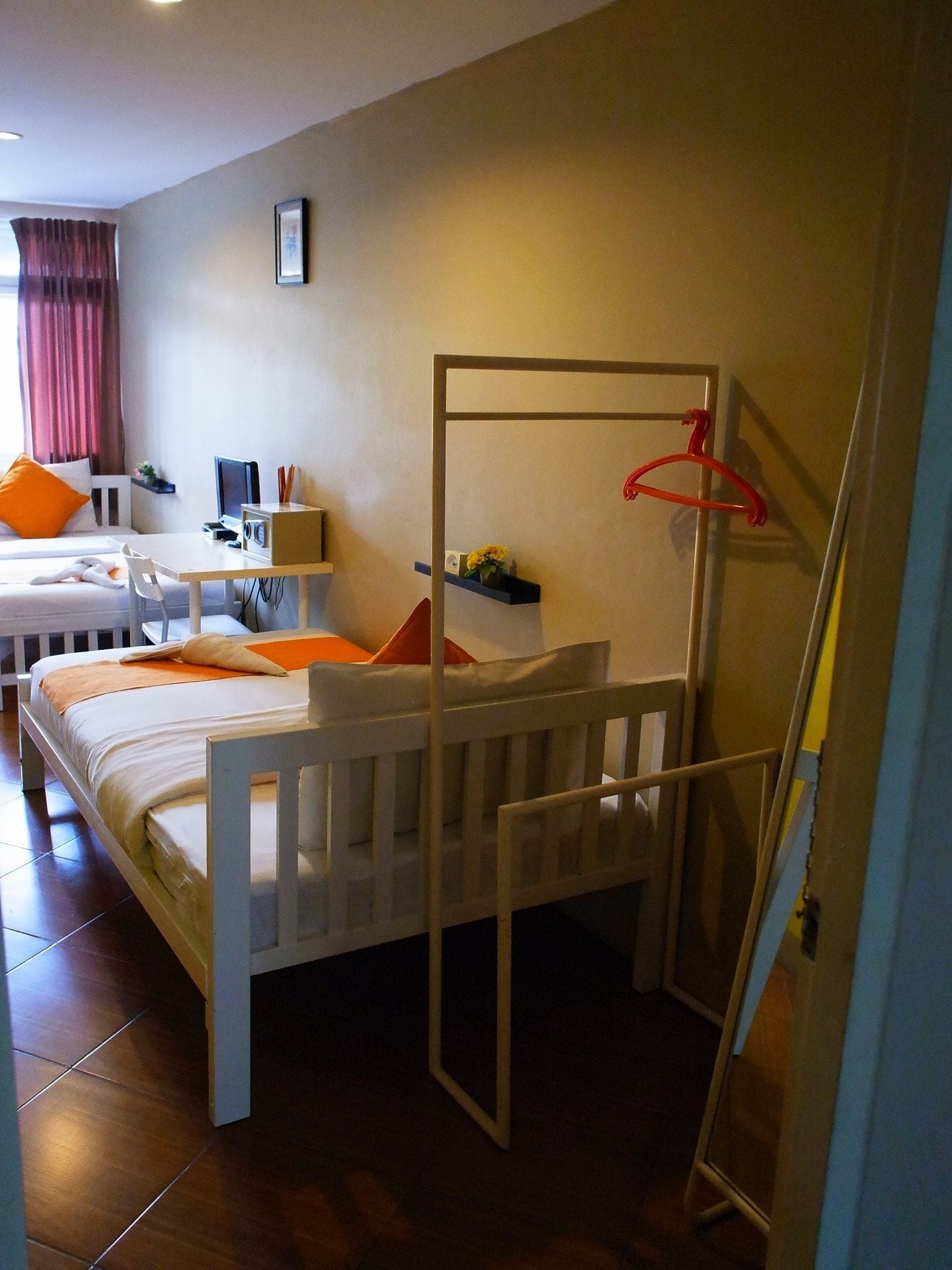 Habitación de hotel con una cama individual, un escritorio con silla, una mesita, un televisor y una estantería con una planta.