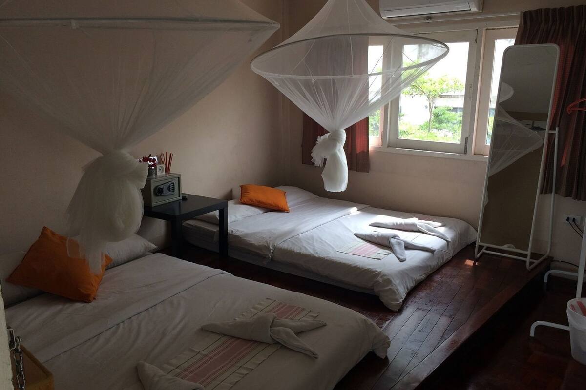 A hotel room with two beds, a bedside table with a radio, a mosquito net, and a window with curtains.