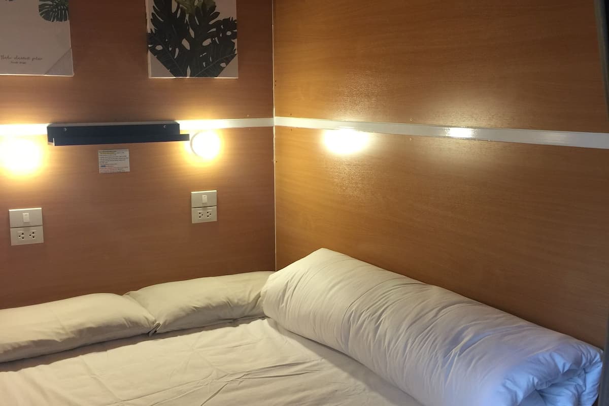 A single bed with white bedding in a room with wooden walls and two wall-mounted light fixtures.