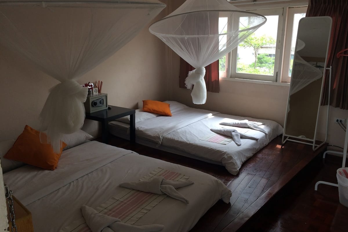A hotel room with two beds, a bedside table with a radio, and a mosquito net over the window.