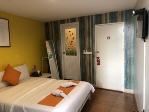 A hotel room with a bed, a mirror, a door with a floral design, and a wall-mounted TV. - VX The Fifty - Hostel (Bangkok)