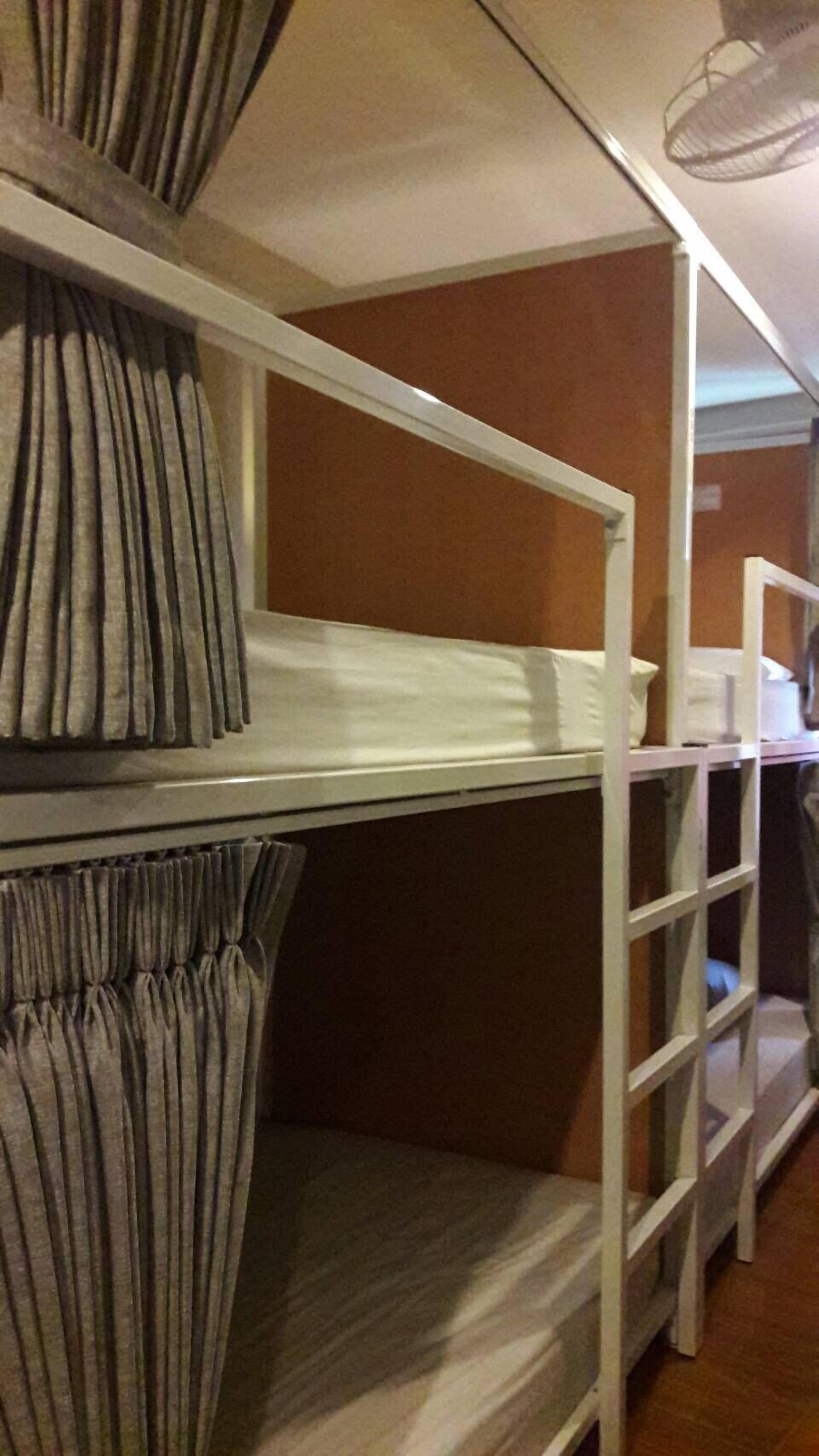A bunk bed with grey curtains, a white ladder, and a wooden floor.