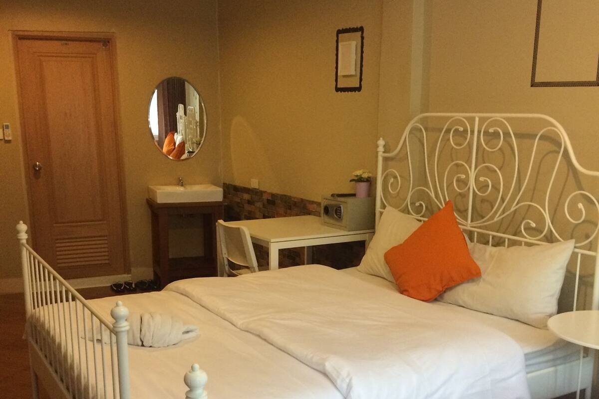 A bedroom with two beds, a bedside table, a mirror, and a small desk with a chair.