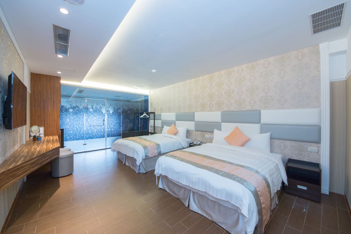 A modern hotel room with two beds, a wooden vanity, a large mirror, and a view of the outdoors.
