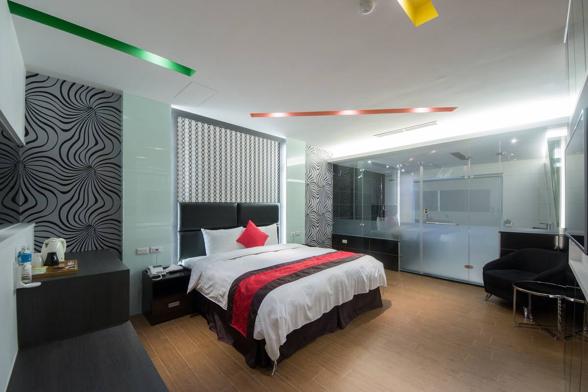 A modern hotel room with a large bed, a desk, and a mirror.
