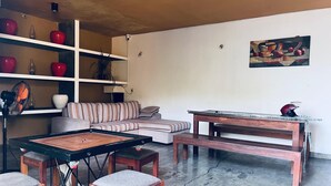 Una sala de estar con un sofá, una mesa de centro y un banco de madera. Hay estantes con objetos decorativos y un cuadro en la pared.