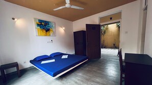 Una habitación con cama, escritorio, silla, ventilador de techo y un cuadro en la pared.