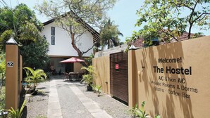 Entrada de un hostal con un cartel de bienvenida, un acceso con reja y un camino que lleva al edificio.