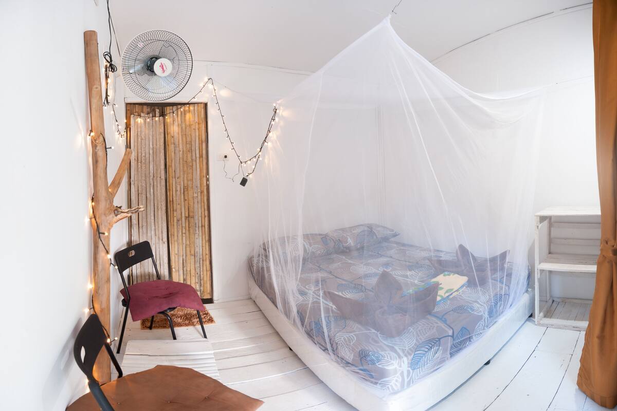 A cozy bedroom with a canopy bed, a wooden door, a chair, and a fan.