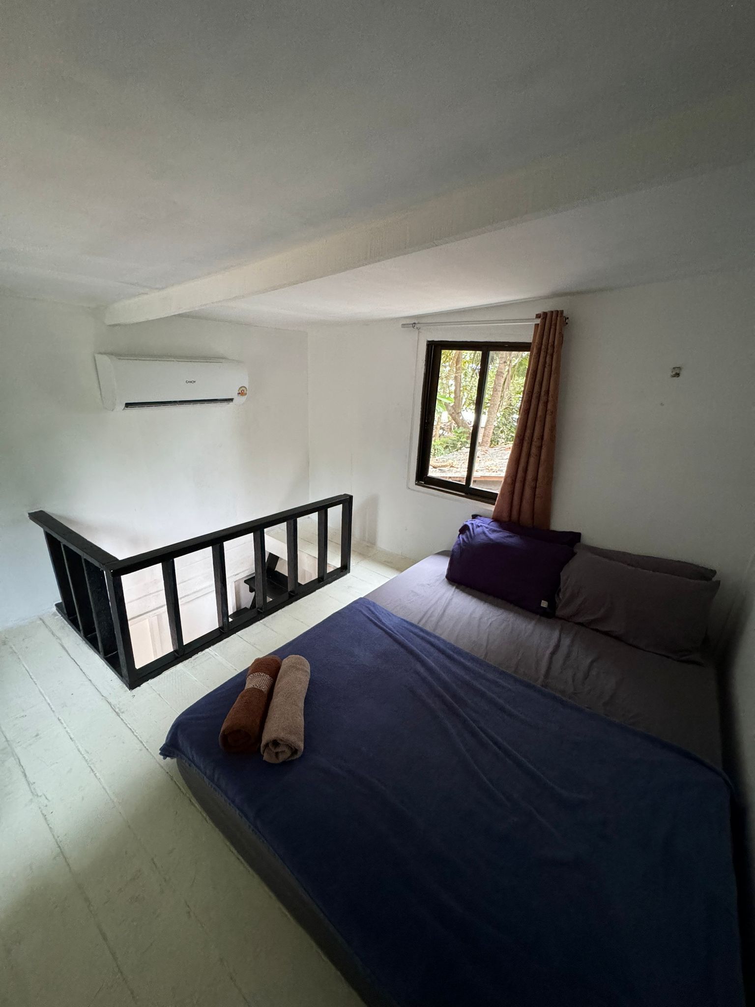 A bedroom with a bed, a window, a balcony, and an air conditioning unit.