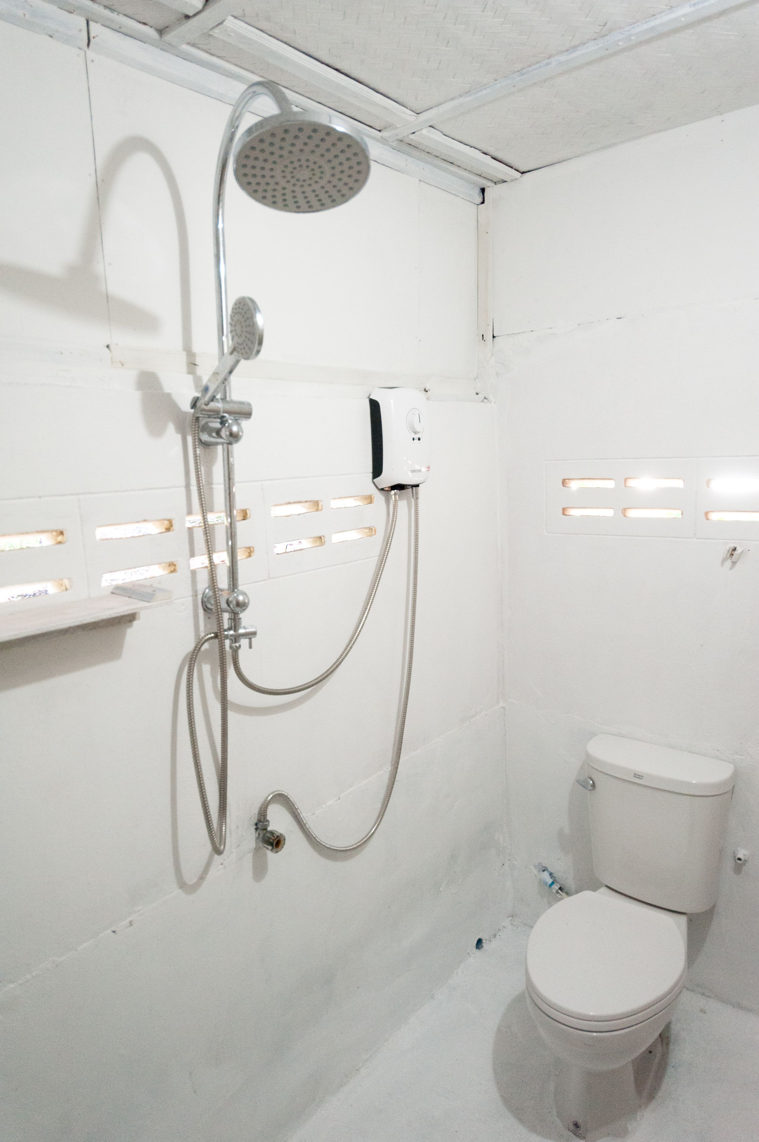 A white bathroom with a shower, toilet, and a wall-mounted electrical outlet.