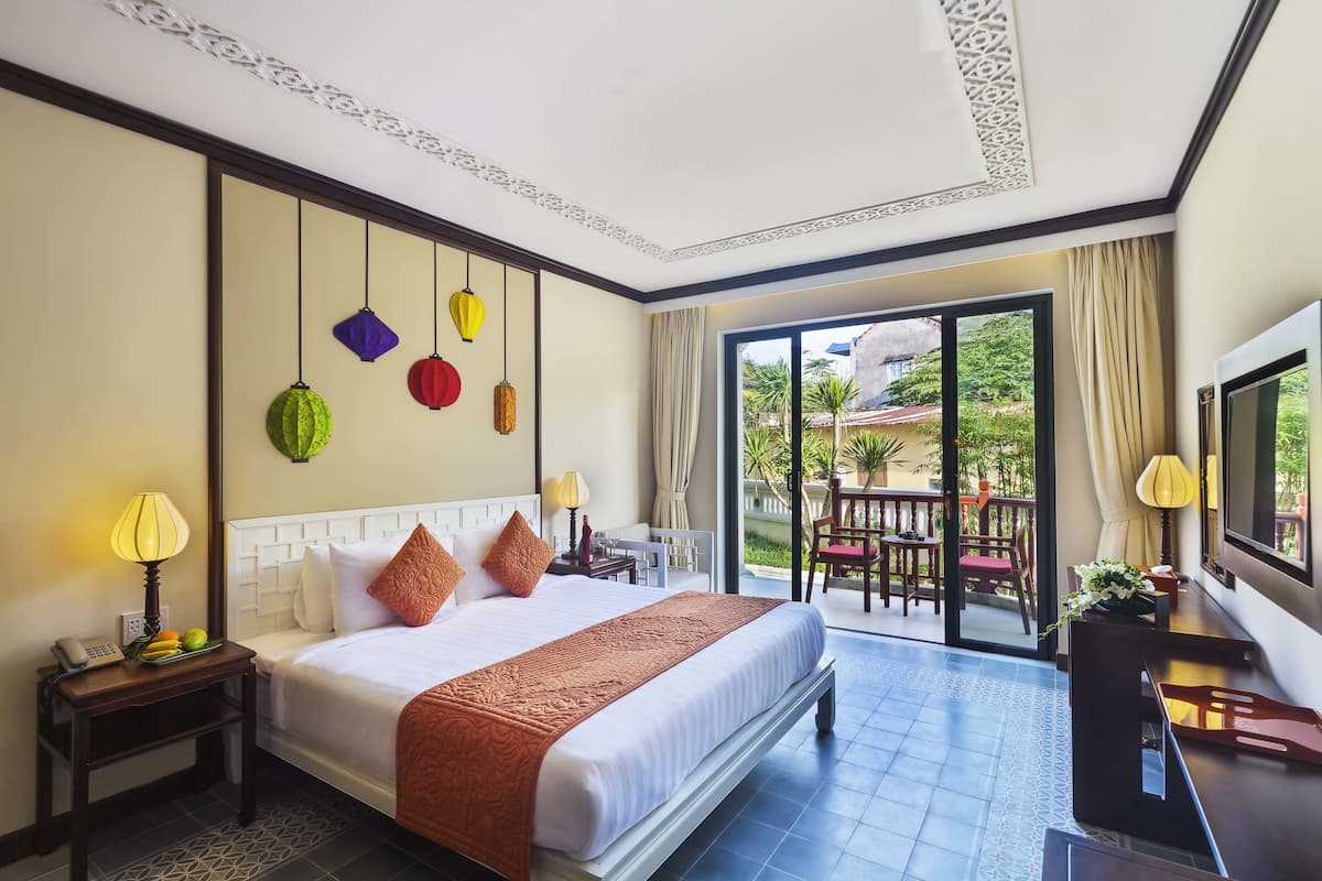 Een hotelkamer met een groot bed, een televisie, een bureau en een balkon met zitplaatsen.