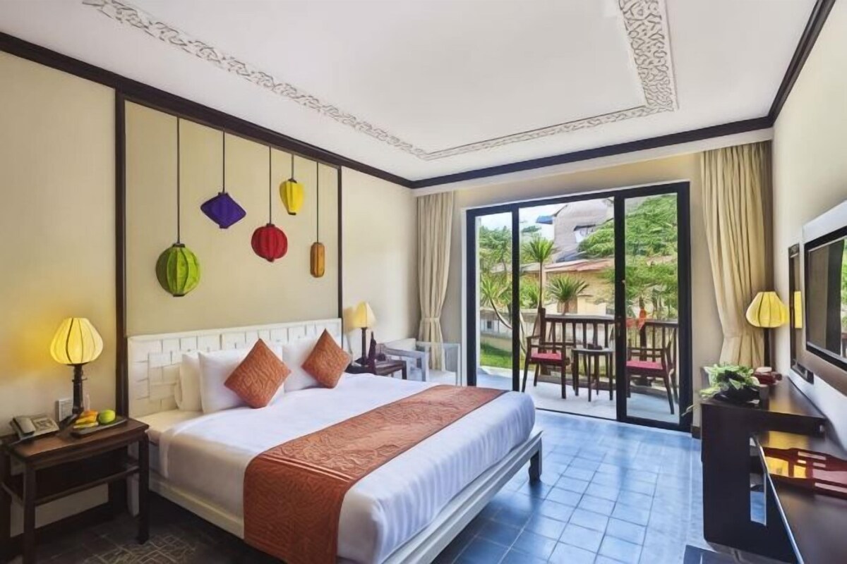 Une chambre d’hôtel équipée d’un lit, d’une télévision, d’un balcon avec mobilier d’extérieur et offrant une vue sur la verdure.