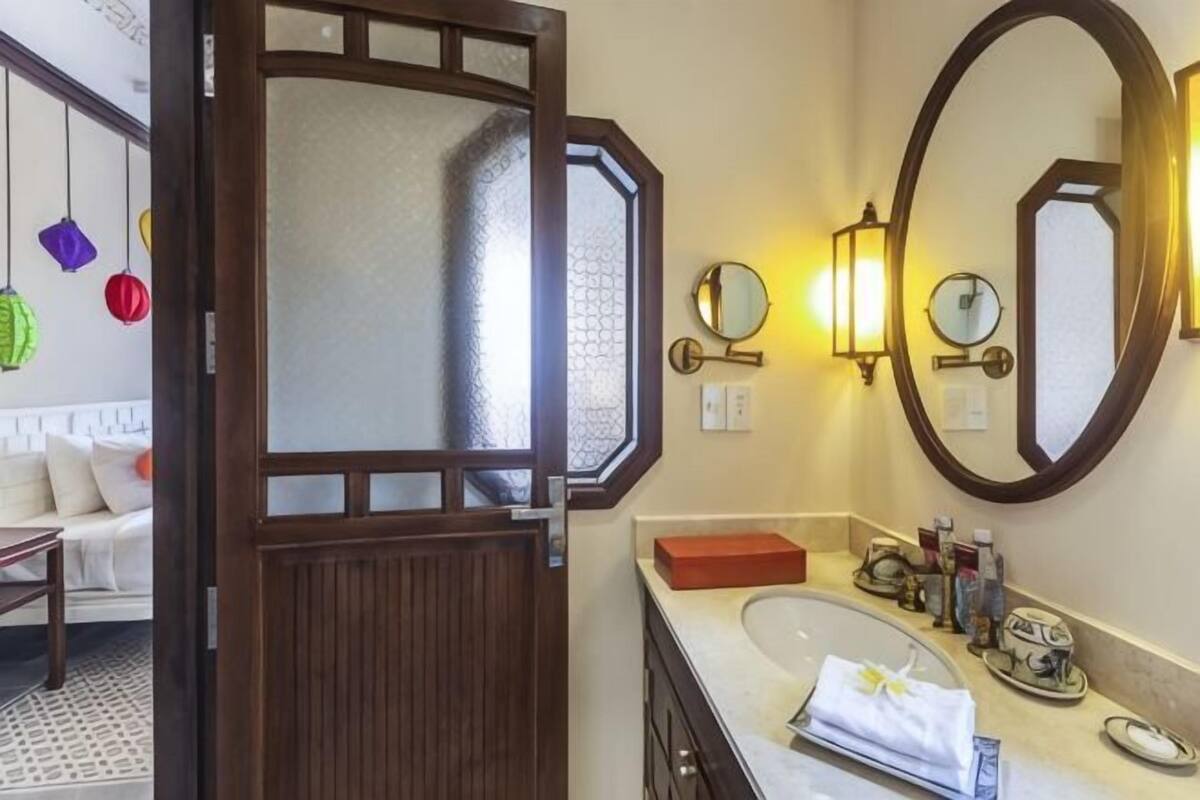 Een hotelbadkamer met een houten deur, een ronde spiegel, een wastafel en een handdoek op het aanrecht.