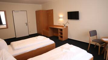 Quarto de hotel com duas camas de solteiro, uma secretária de madeira, uma cadeira, televisão e guarda-roupa.