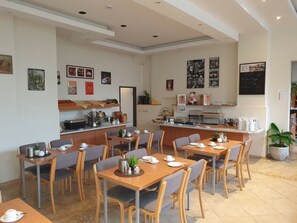 A cafe with multiple tables and chairs, a coffee bar, and various wall decorations. - City-Pension Magdeburg (Magdeburg)