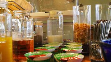 Una mesa de buffet con diversas opciones de comida y bebida, incluyendo frascos de pepinillos, dispensador de leche y recipientes de yogur.