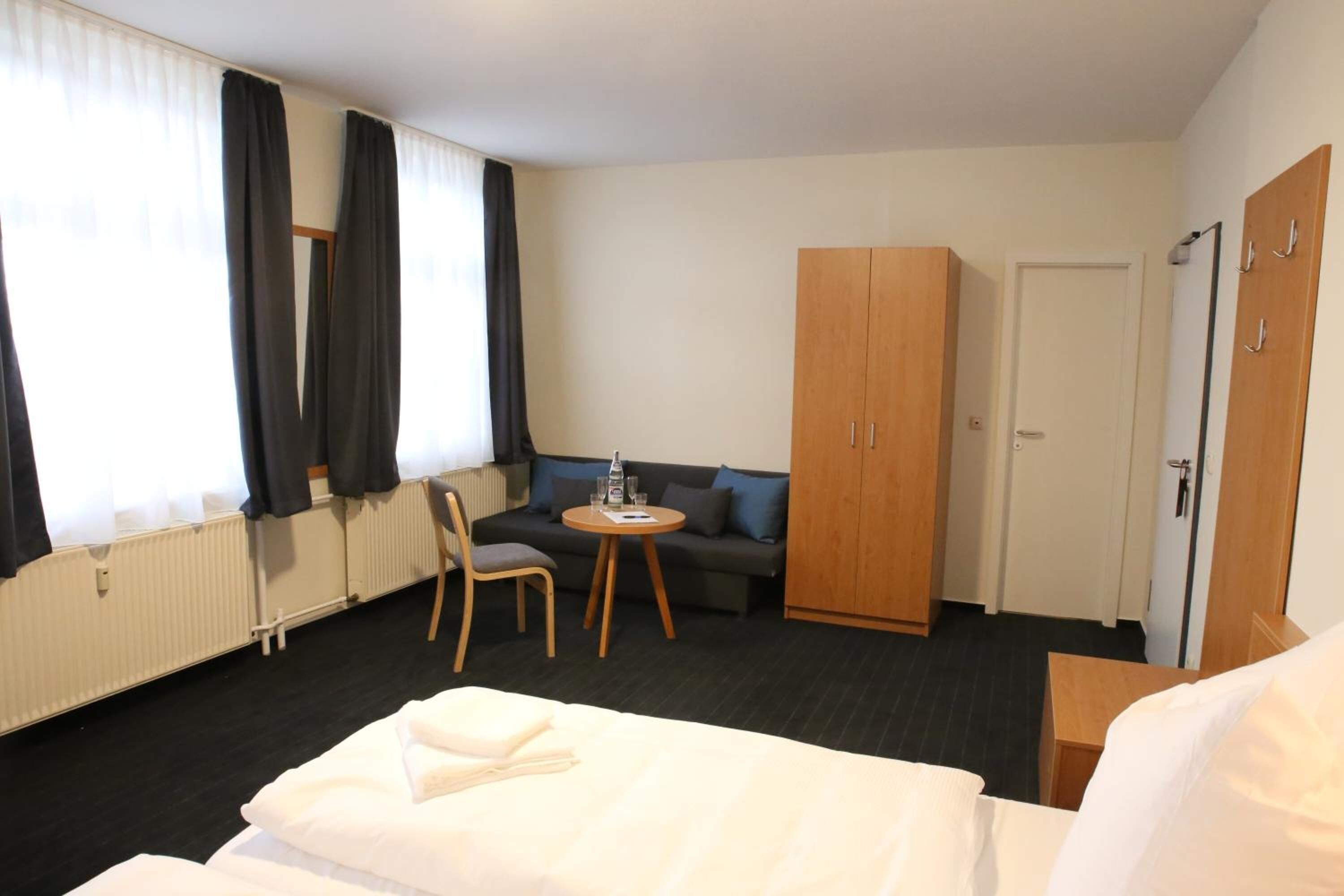A hotel room with a bed, a sofa, a small table, a chair, and a wardrobe.