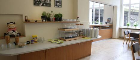 Una cafetería con mostrador, estanterías con plantas y un amplio ventanal.