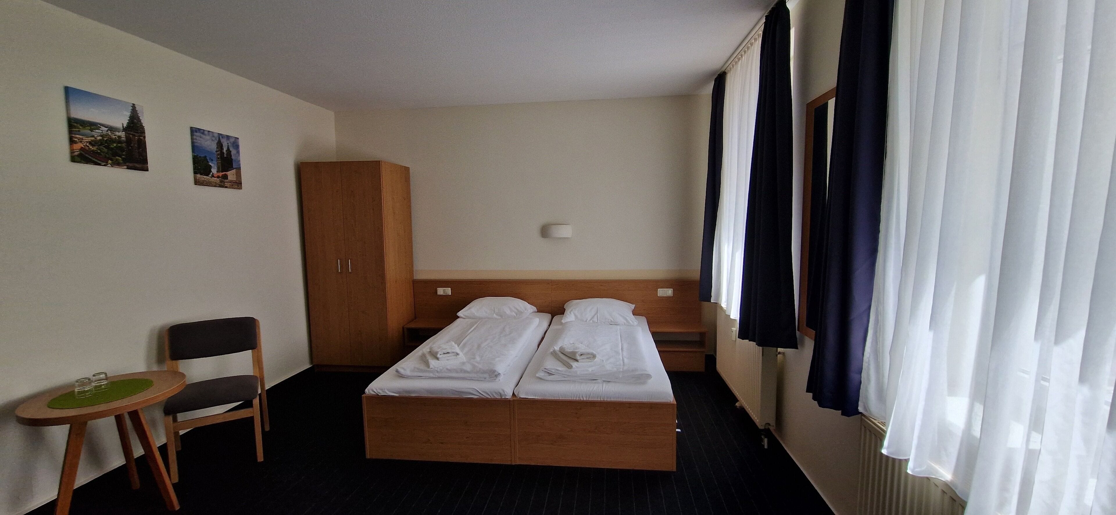 Ein Hotelzimmer mit Doppelbett, einem Holzschrank, einem kleinen Tisch mit Gläsern und einem Stuhl.