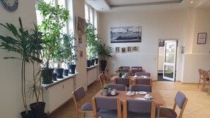 A dining area with tables set for four, surrounded by potted plants, and a large window providing natural light. - City-Pension Magdeburg (Magdeburg)