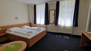 Une chambre d’hôtel comprenant un lit, un bureau, une chaise, une petite table avec des verres et une poubelle.