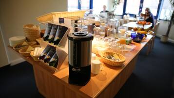 A buffet setup with a coffee machine, serving trays, and a variety of food items.