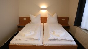 A double bed with white linens and pillows, a nightstand with a lamp, and a window with curtains. - City-Pension Magdeburg (Magdeburg)