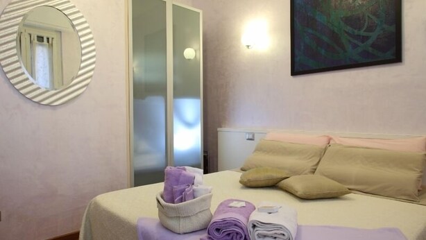 A hotel room with a bed, a mirror, a painting, and a towel rack. - Gala B&B (Rome)