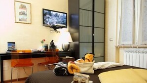 A hotel room with a bed, a desk with a computer, a chair, a lamp, and a window with curtains. - Gala B&B (Rome)