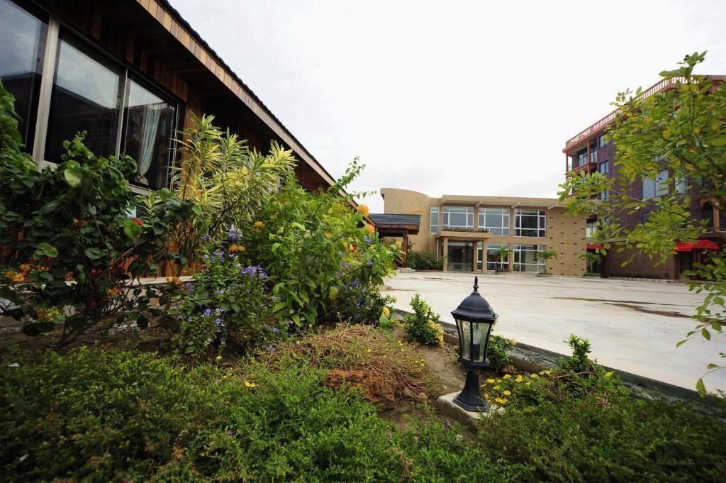 A courtyard with a building featuring large windows and a well-maintained garden with various plants and a lantern.