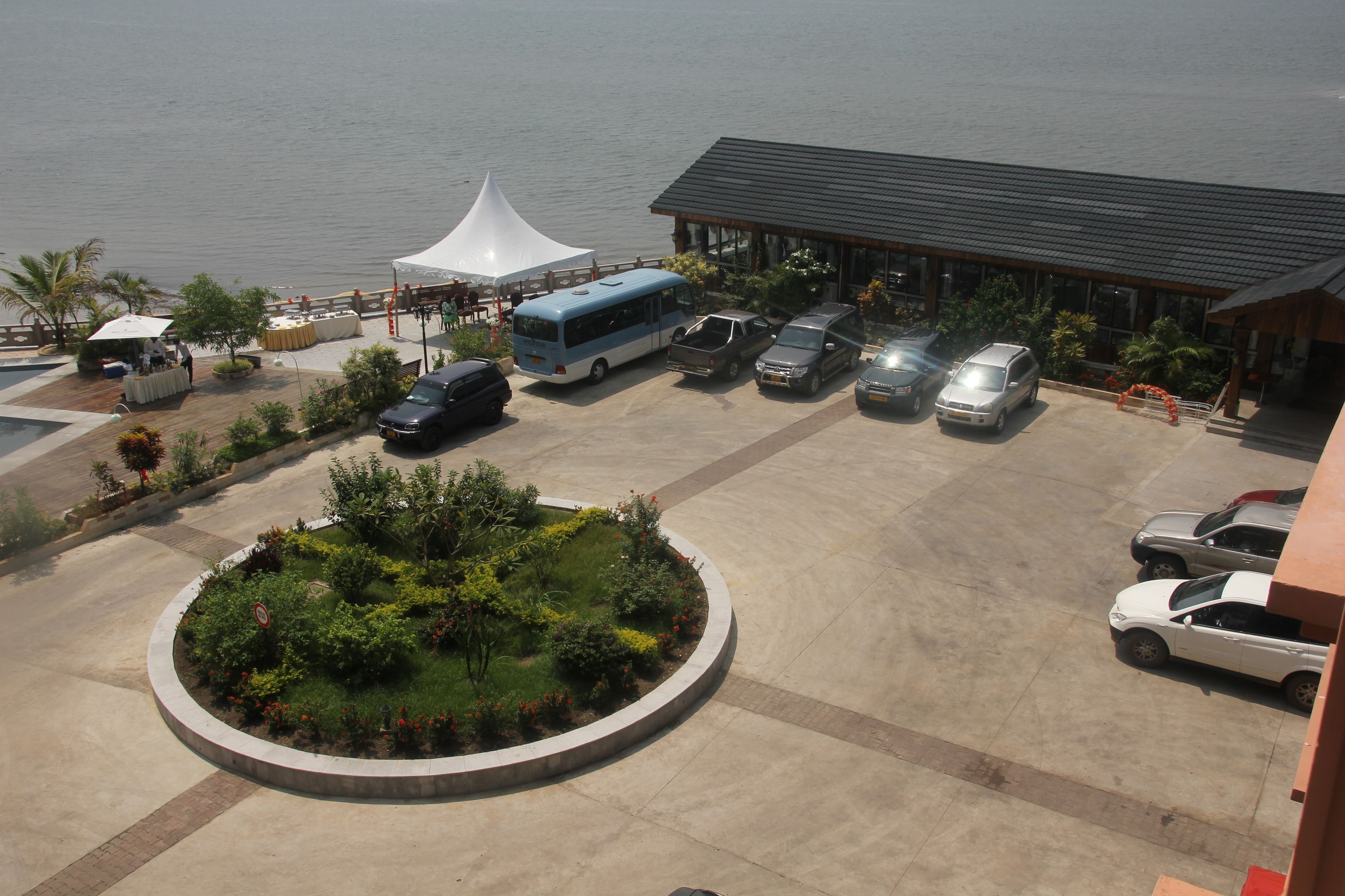 A parking area with a bus, cars, and a building with a roof.