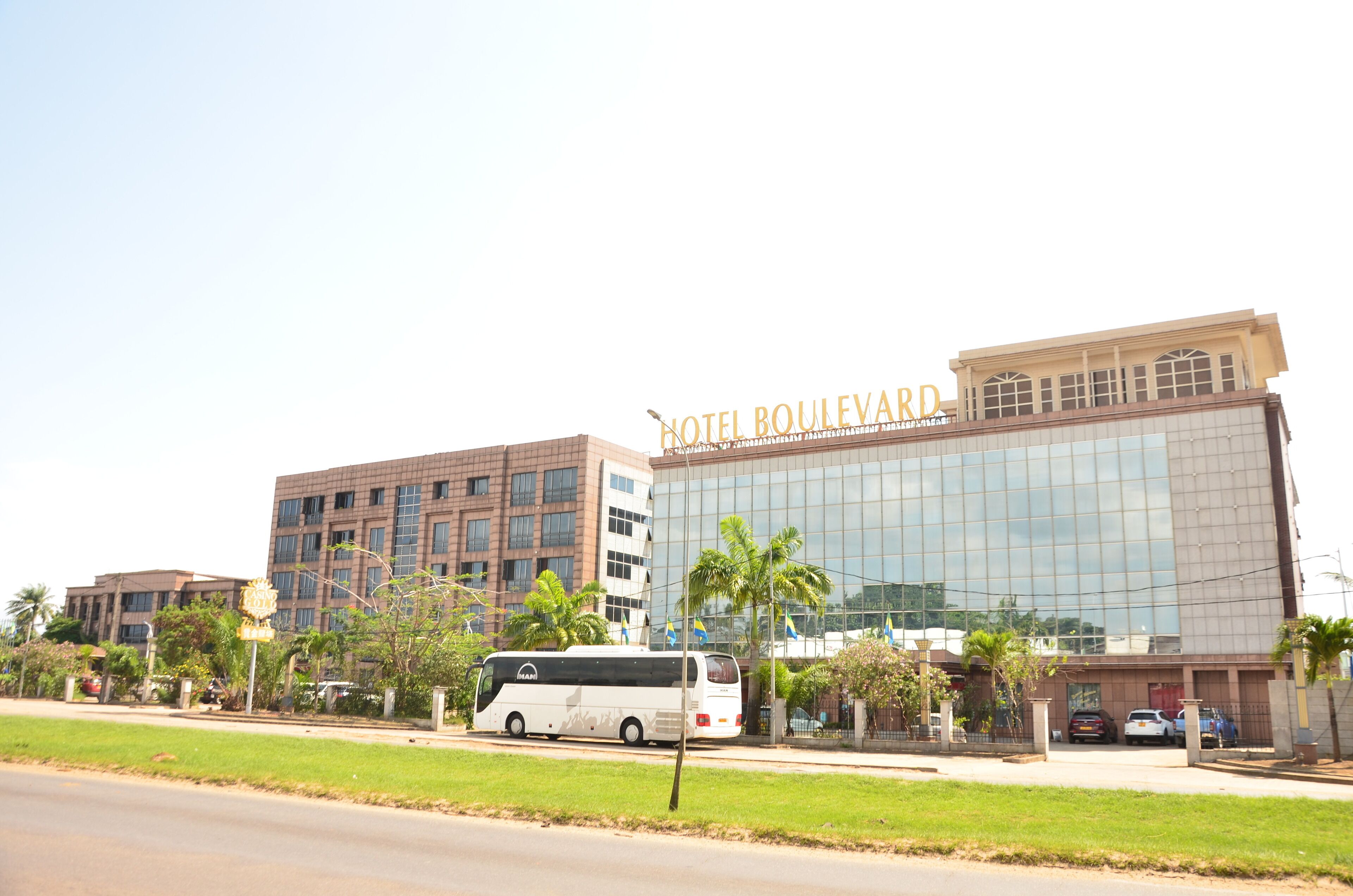 A modern hotel with a glass facade, a bus parked in front, and palm trees.