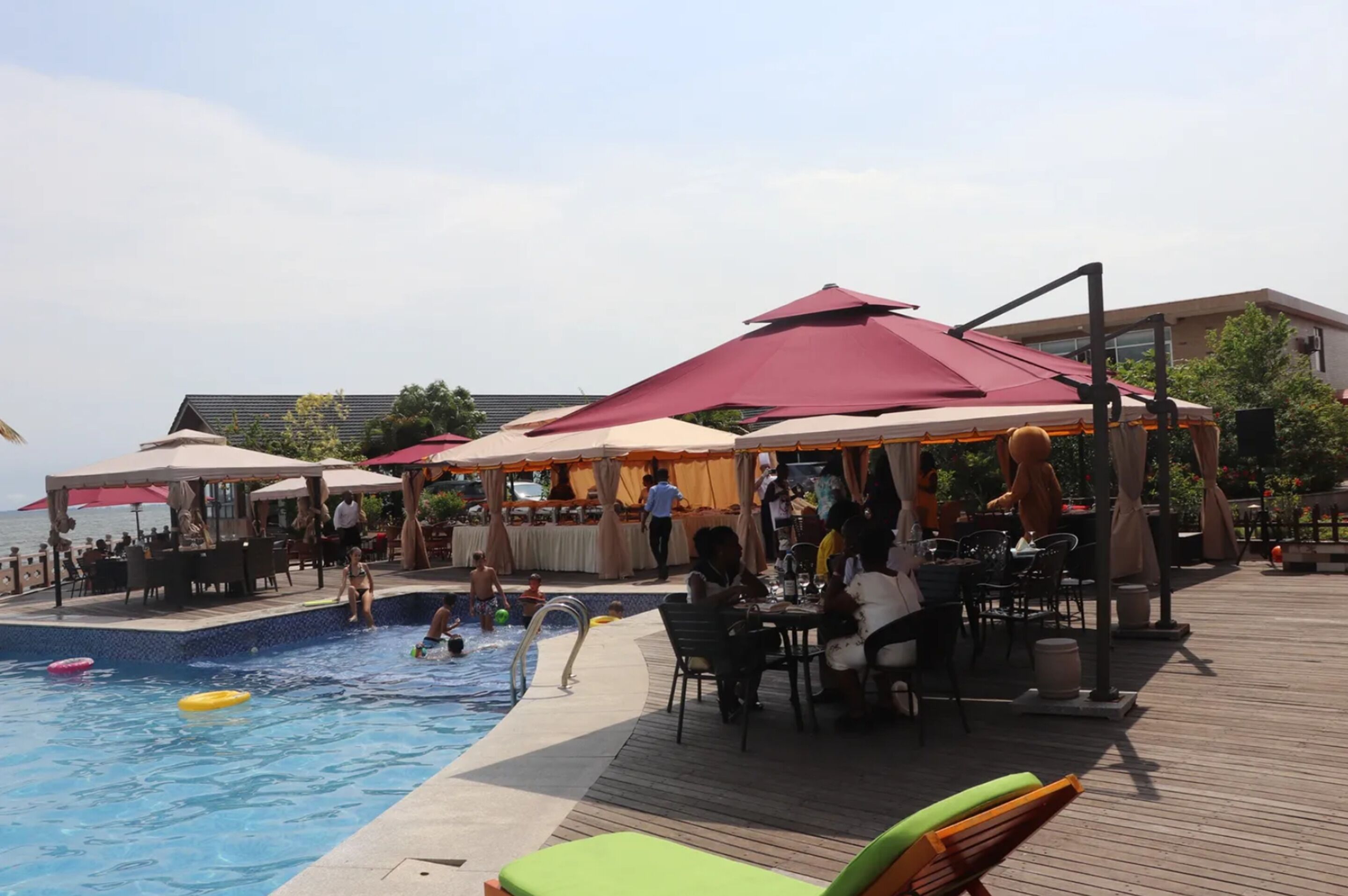 A poolside area with a wooden deck, lounge chairs, and umbrellas providing shade.