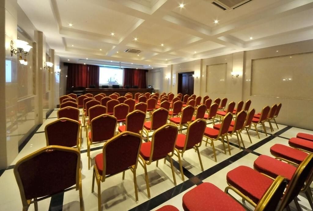 Une salle de conférence avec des rangées de chaises rouges et une scène équipée d’un projecteur.