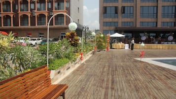 A wooden deck with a bench, surrounded by plants and flowers.